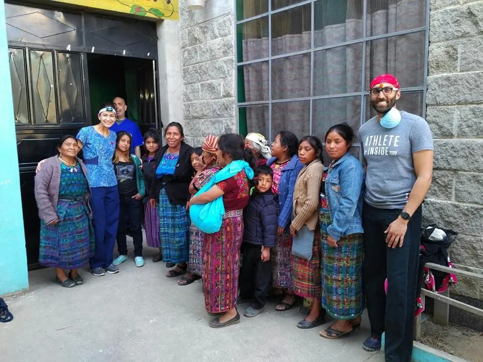 Dental team members standing with a group of women and children outside a building